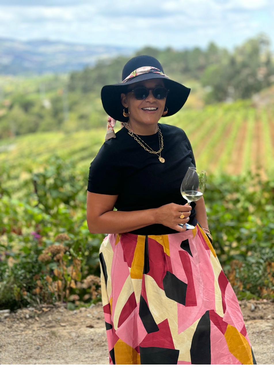 Jamaica smiling in a vineyard, floppy hat, wine glass in hand